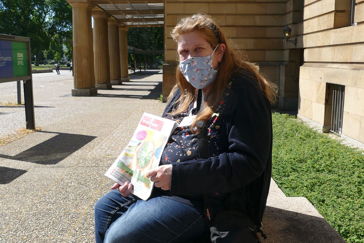 Frau mit langen rotbrauen Haaren und Mundschutz sitzt vor der Oper