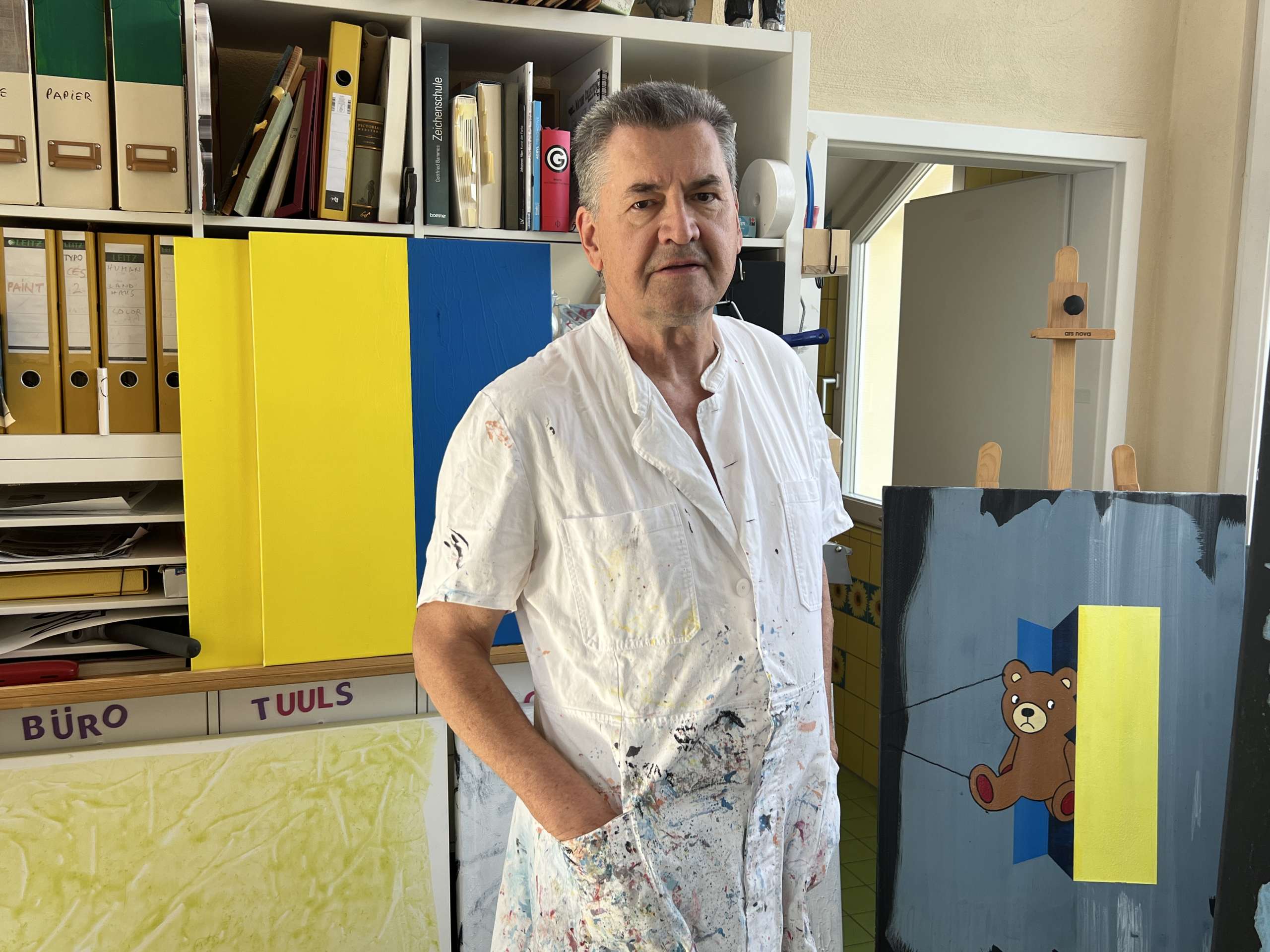 Der Künstler Rolf Lorenz mit farbbeschmiertem Kittel vor einem Werk