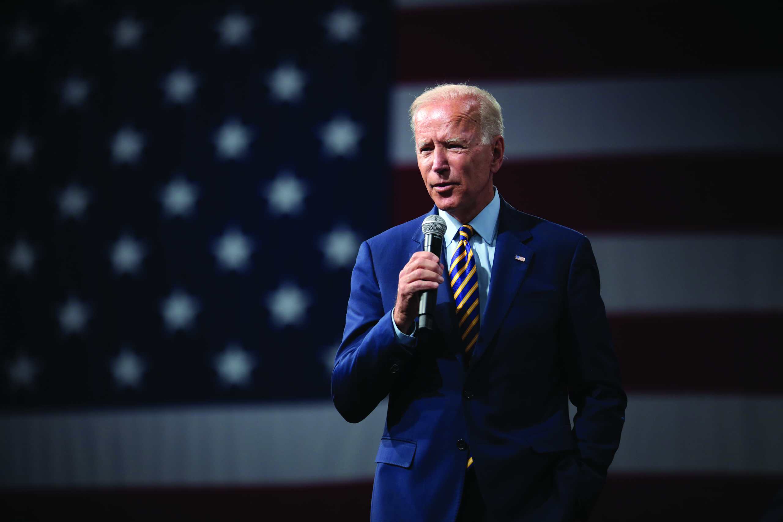 Joe Biden mit einem Mikrofon in der Hand vor eine US-Flagge