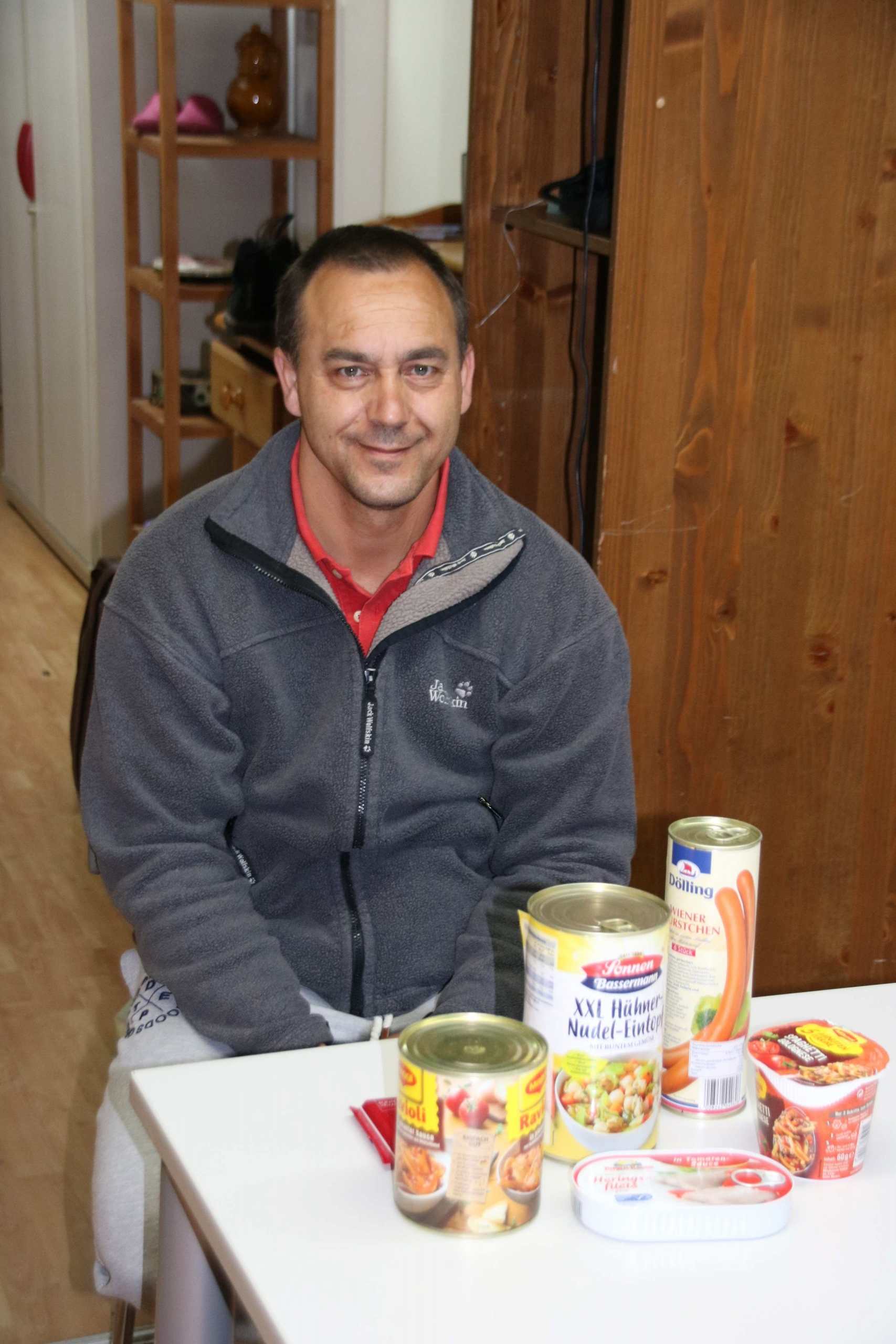 Trott-war-Verkäufer sitzt an Tisch mit den von der Spende gekauften Konserven